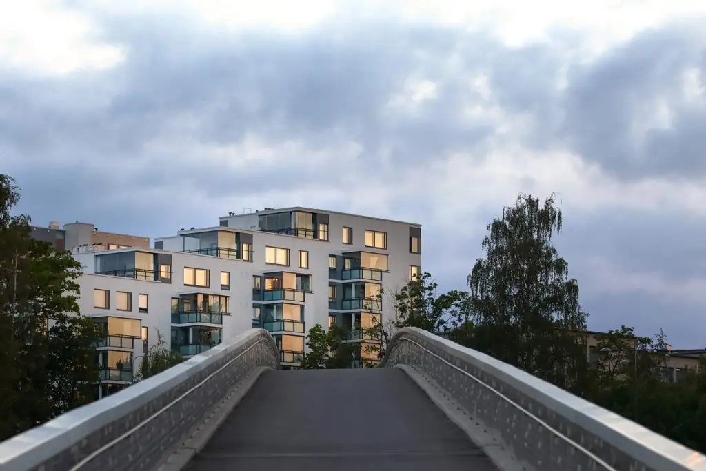 Moderni kerrostalo lasiparvekkeilla kävelysillan päässä iltahämärässä.